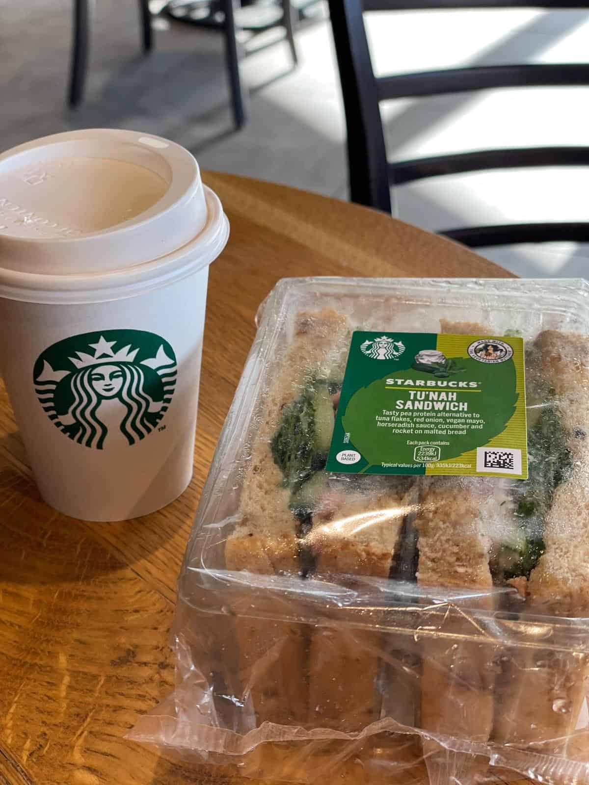 A cup of starbucks of coffee and a sandwich