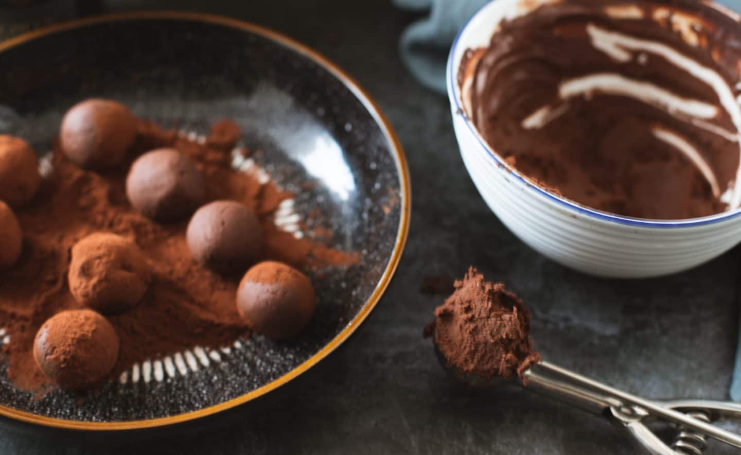 A bowl of truffle mixture, with some truffles being rolled in cocoa powder