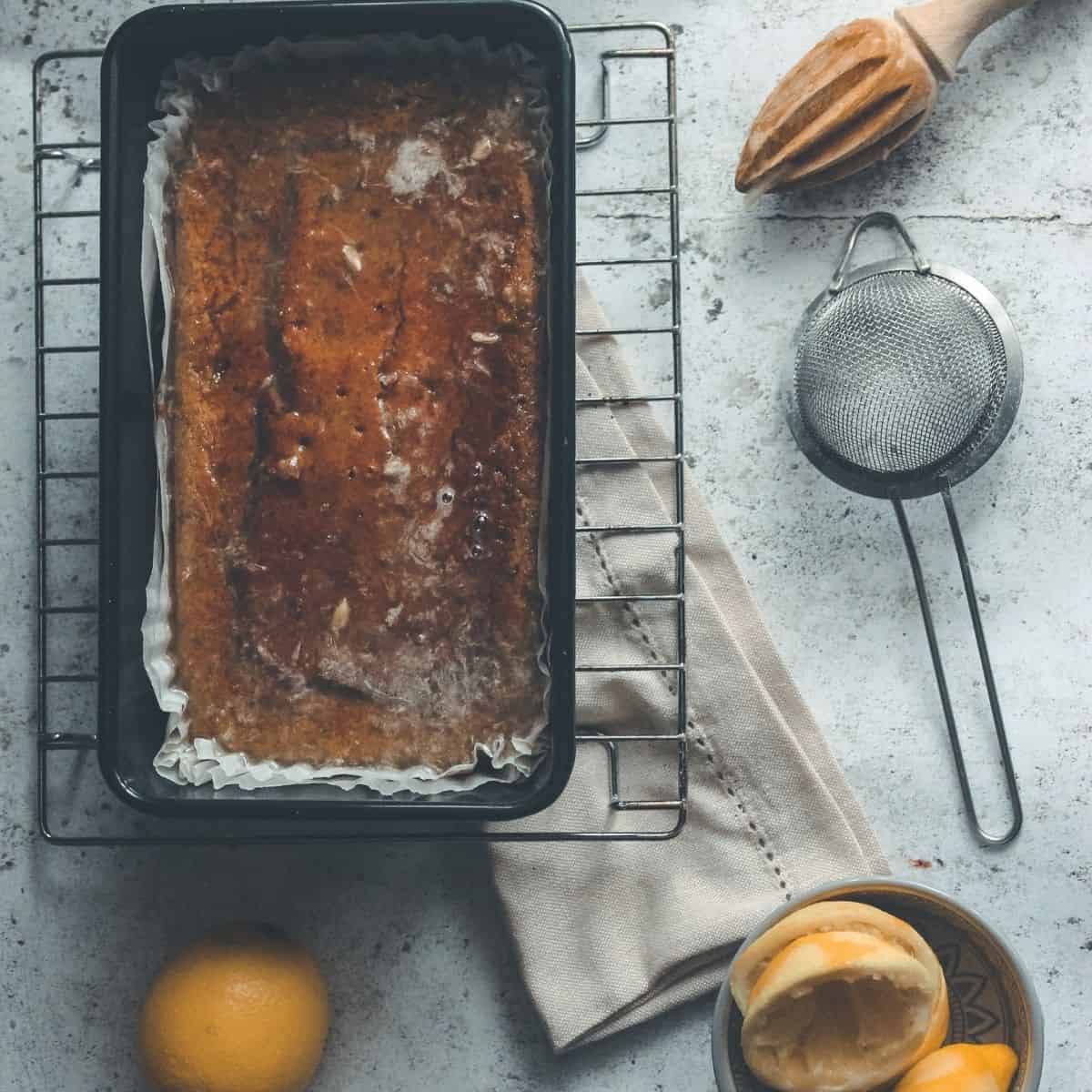 A lemon drizzle cake surrounded by lemons and a juicer