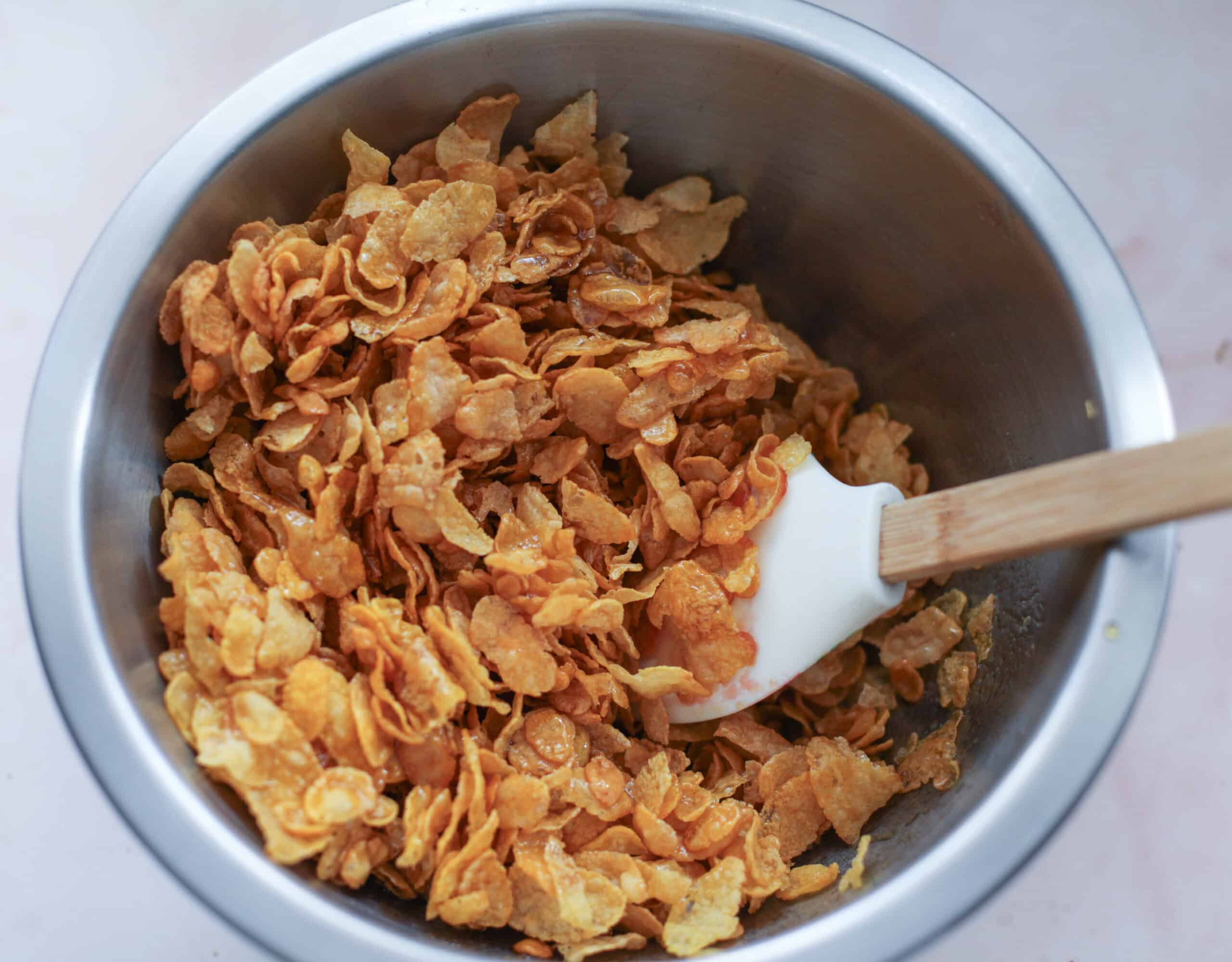 Stirring butter and golden syrup into cornflakes in a mixing bowl.