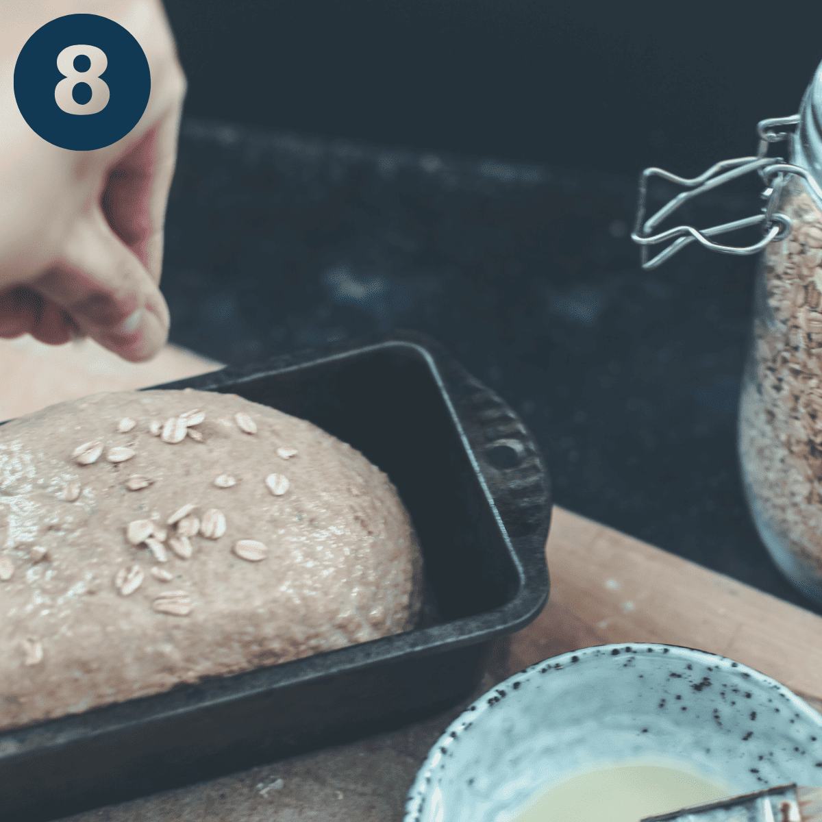Placing oatmeal dough in a loaf tin and sprinkling with oats.