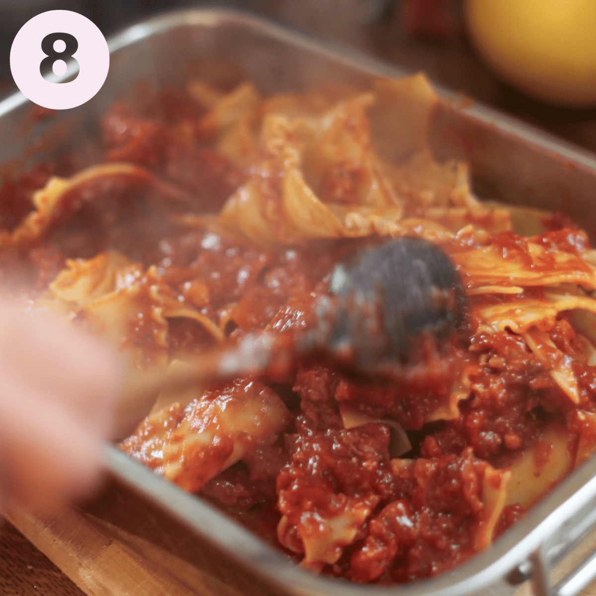 Mixing cooked lasagne pieces into the marinara sauce.