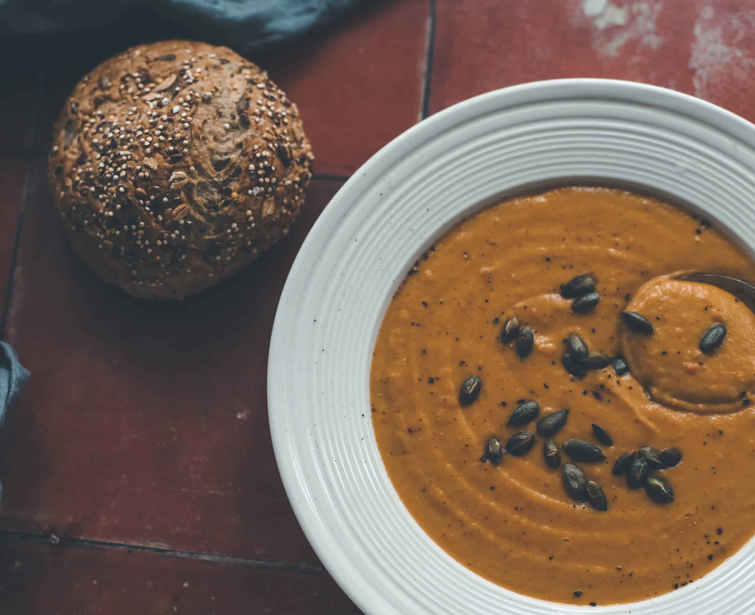A bowl of butternut soup with a bread roll.