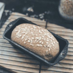 A loaf pan with a loaf of oatmeal bread in it.